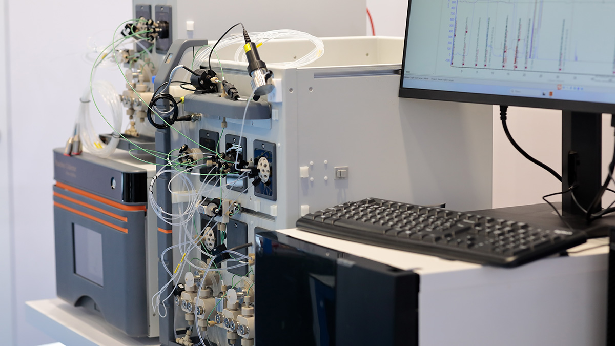 A high-performance liquid chromatography (HPLC) instrument with a computer monitor displaying chromatogram peaks. Non-targeted screening workflows analyze patterns in this kind of data to identify PFAS compounds that are not on the targeted compound list of standardized methods like EPA Method 1633.