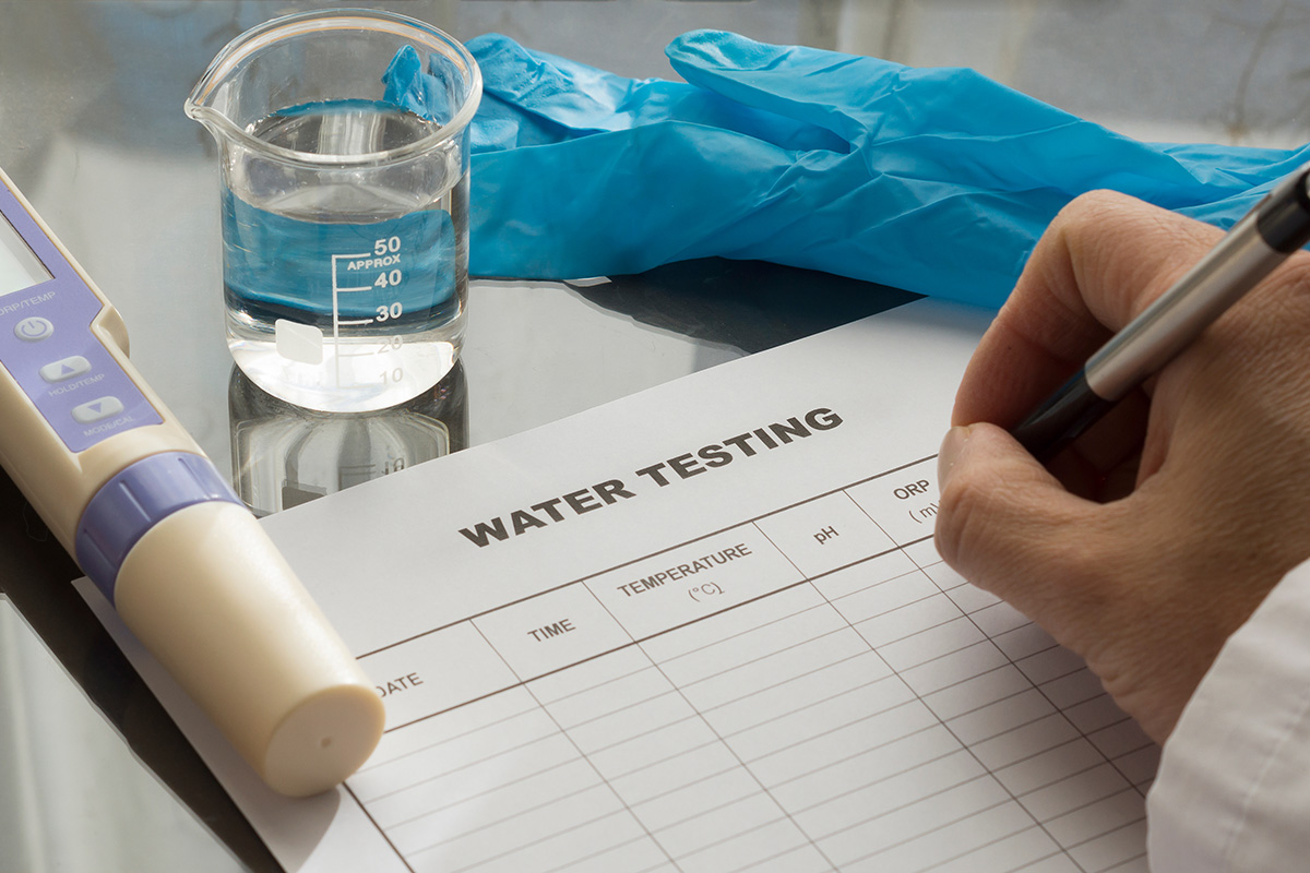 Water quality technician recording results on a compliance monitoring form alongside a pH meter and water sample — PFAS drinking water testing under state and federal regulatory standards